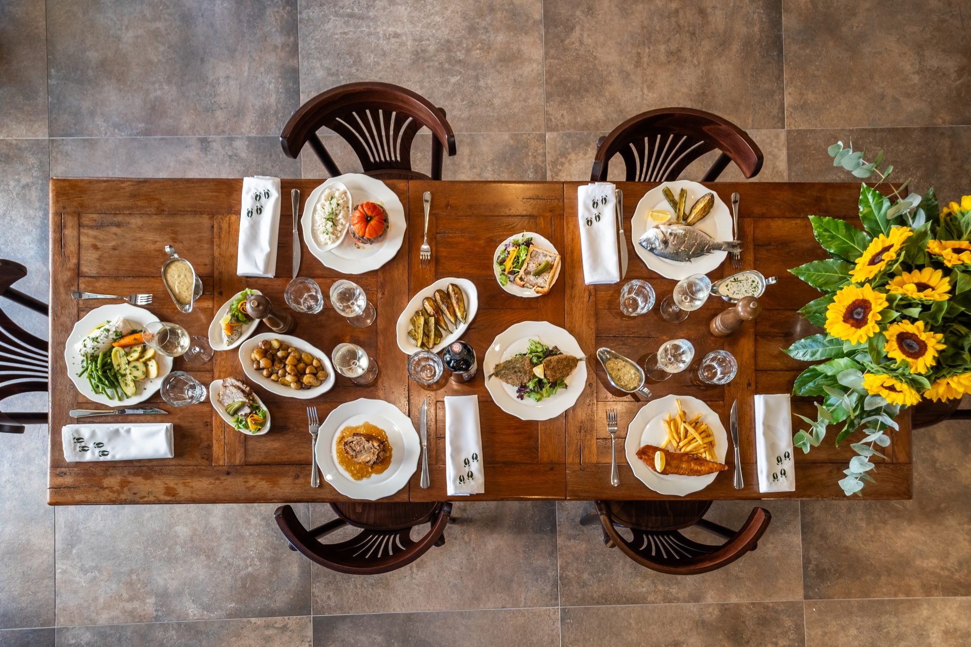 Une table dressée au Sanglier Rieur, garnie de plats à partager et de fleurs.
